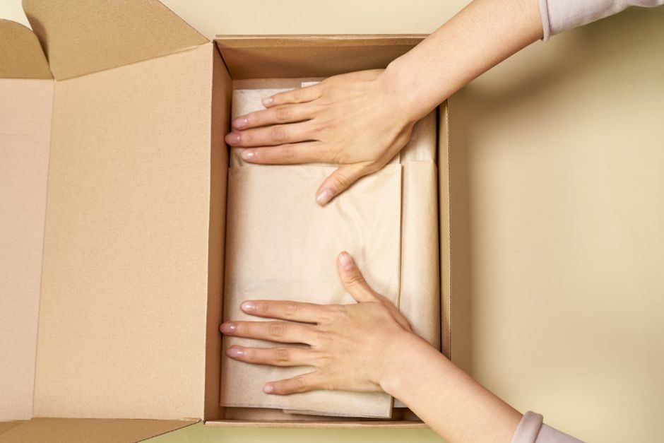 Close-up of hands packing a cardboard box with care using parchment paper.