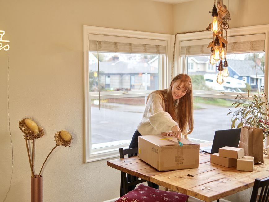 A woman joyfully unboxing a package in a cozy home office setting.